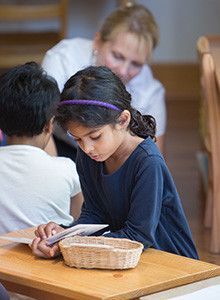 A little girl is sitting at a table reading a book.