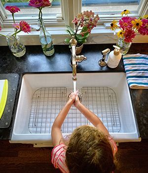 A little girl is washing her hands in a kitchen sink.