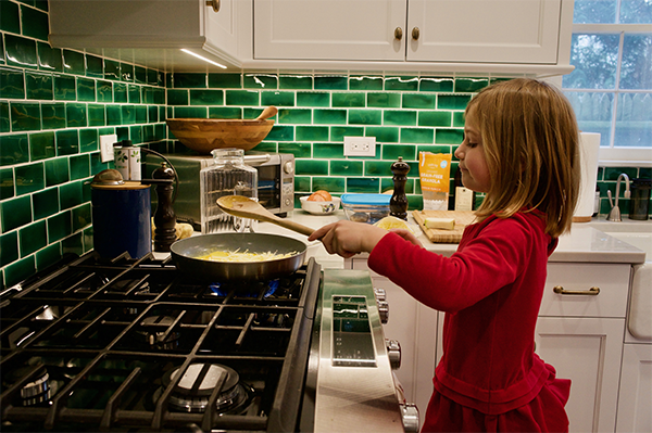 A young girl cooks at a stove during the holidays.