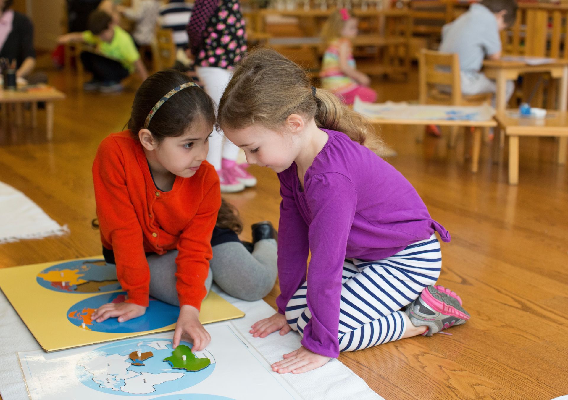 Two Montessori children are sitting on the floor working with a puzzle.