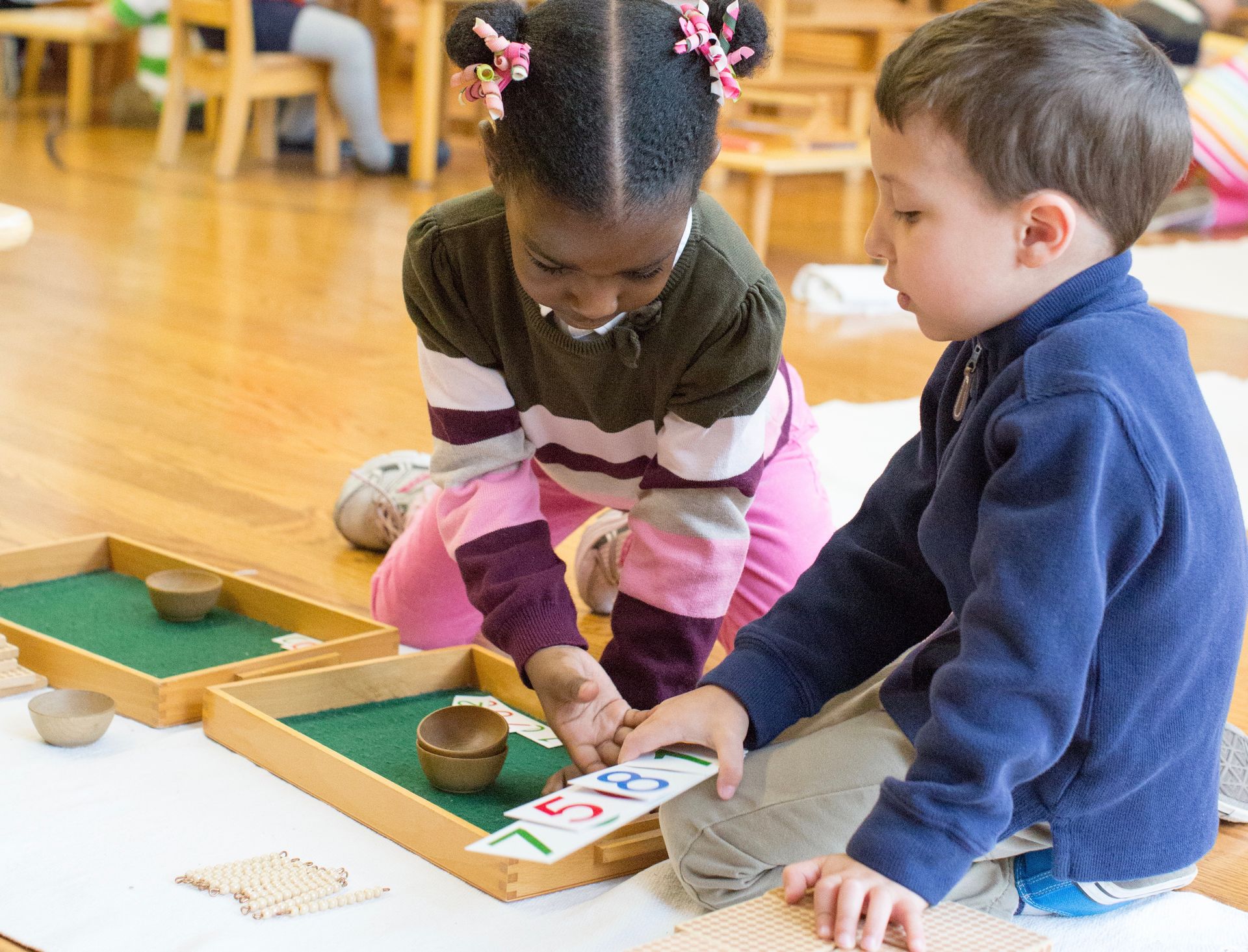 Montessori children are sitting on the floor working with number materials