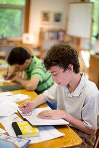 A boy is sitting at a desk in a classroom reading a book.