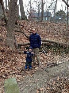 A man and a little boy are standing next to each other in the woods.