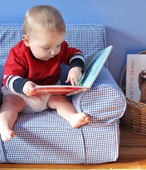 A baby is sitting on a chair reading a book 