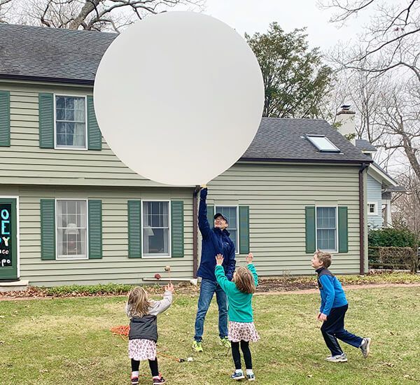 A group of children are playing with a large white balloon in front of a house.