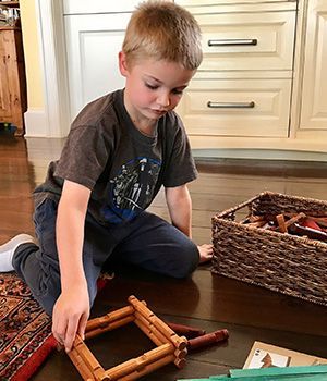 A boy sitting on the floor palying with small wooden logs