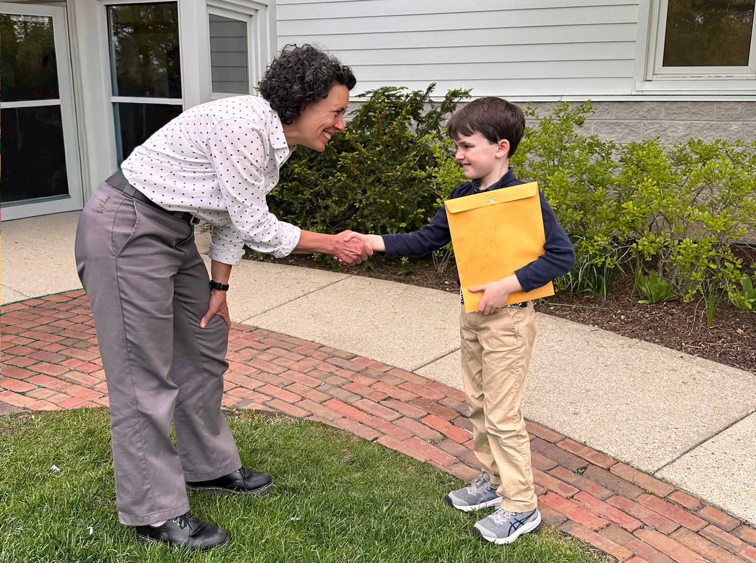 A smiling Montessori teacher shakes hands with a smiling elementary student