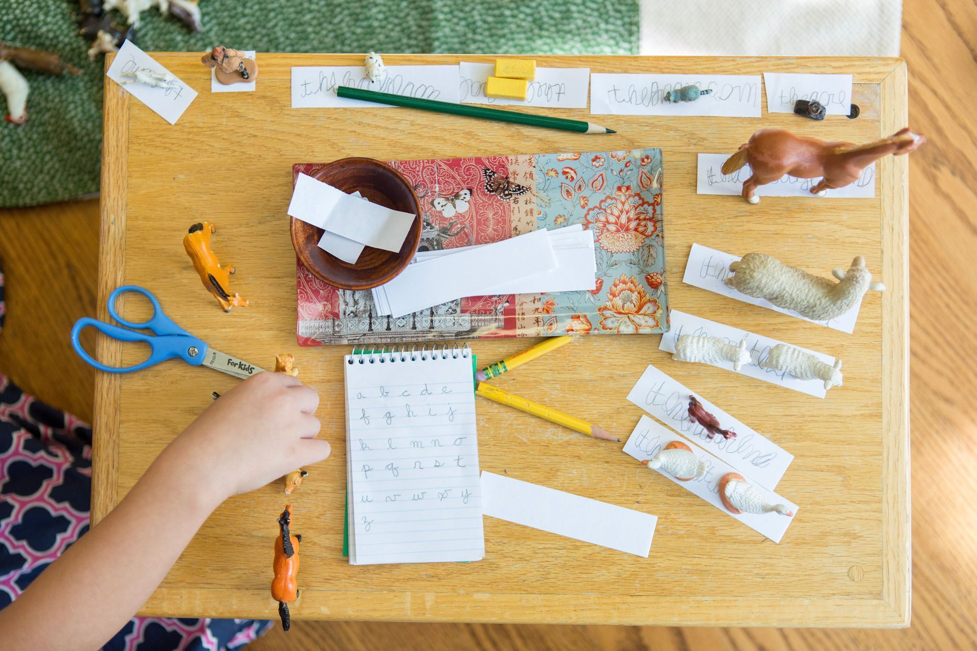 A Montessori floor desk covered with figurines of farm animals and slips of paper with student's writing