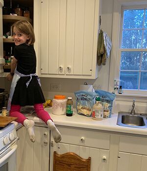 A little girl is sitting on a counter in a kitchen.