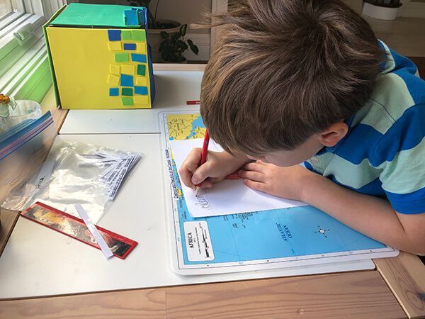 A young boy is sitting at a desk writing on a piece of paper