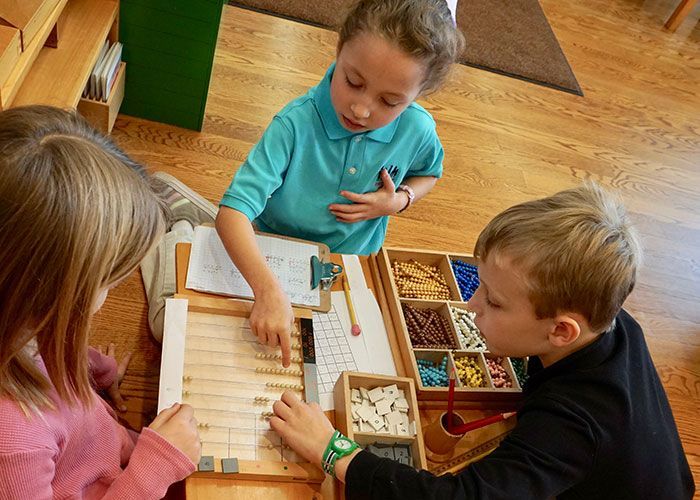 A group of children are sitting around a table working with Montessori Materials