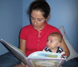 A woman is reading a book to a baby.