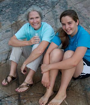 A woman and a young girl are sitting on a rock.