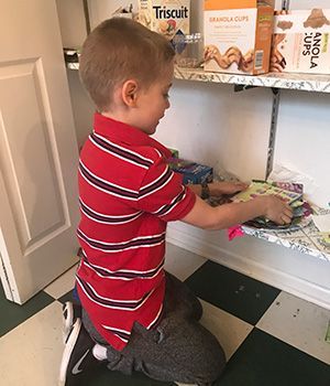 A young boy is kneeling down in front of a shelf with a box of triscuit on it