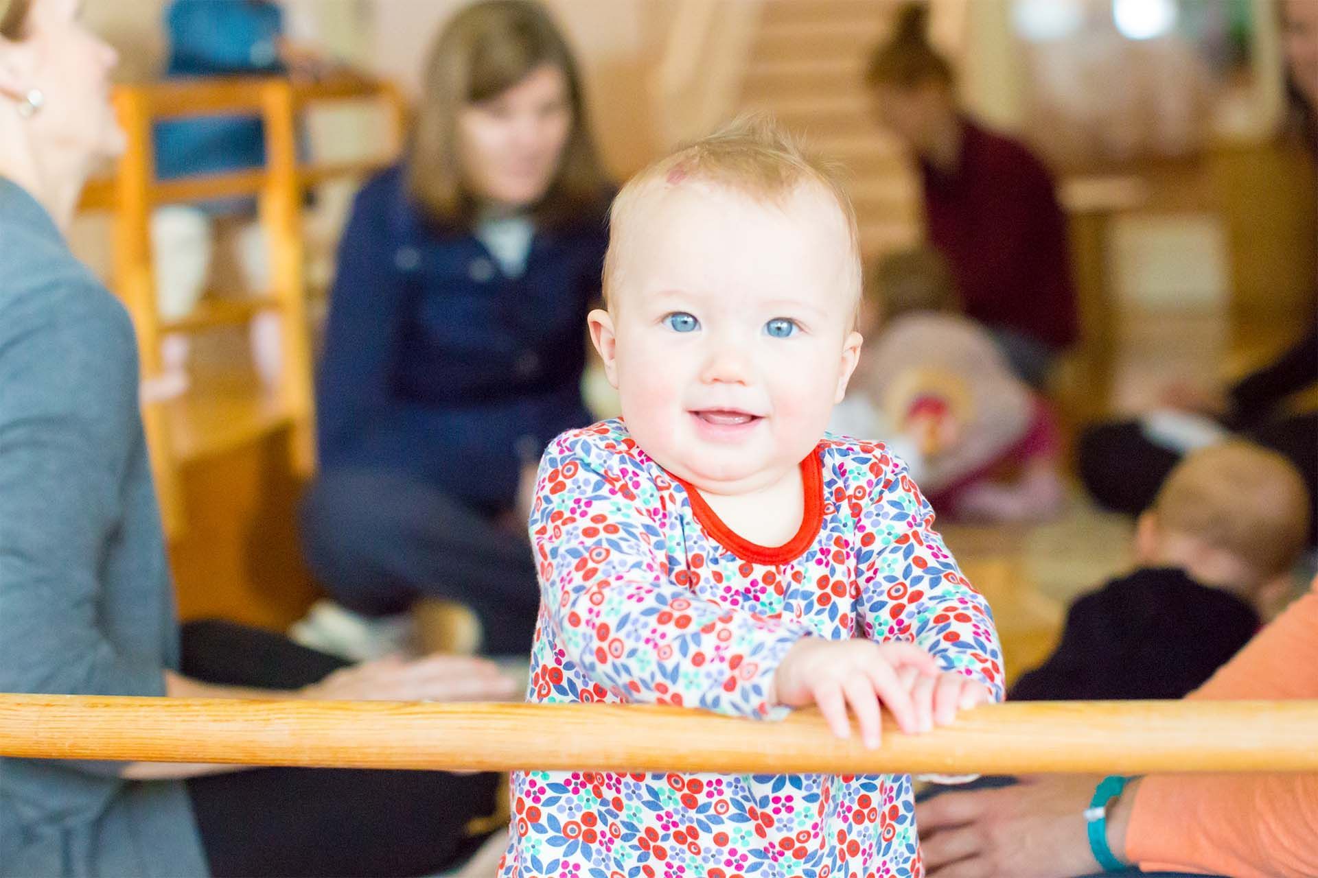 Montessori child is standing and holding on to a wooden railing in a room.