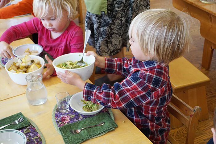 A boy and a girl are sitting at a table eating from bowls.