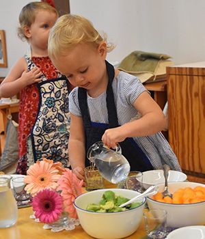 A little girl is pouring water into a bowl of vegetables.