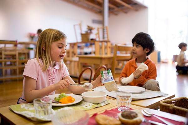 A boy and a girl are sitting at a table eating food.