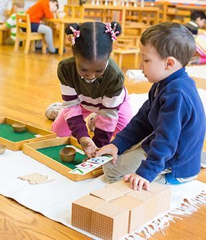 A boy and a girl sitting on the floor working with Montessori math materials