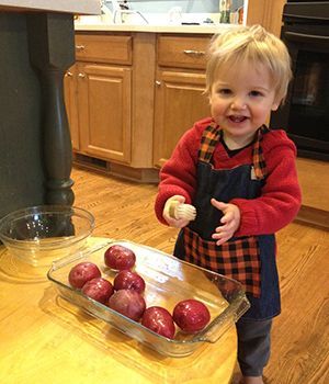 A little boy is standing in front of a tray of potatoes.