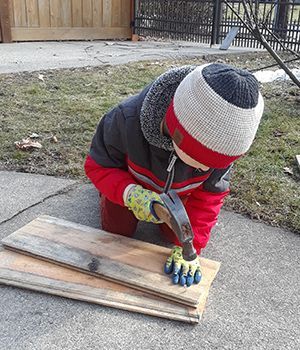 A young boy is using a hammer to hammer a piece of wood.