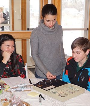 A group of young people are sitting at a table looking at a box of coins and bills.