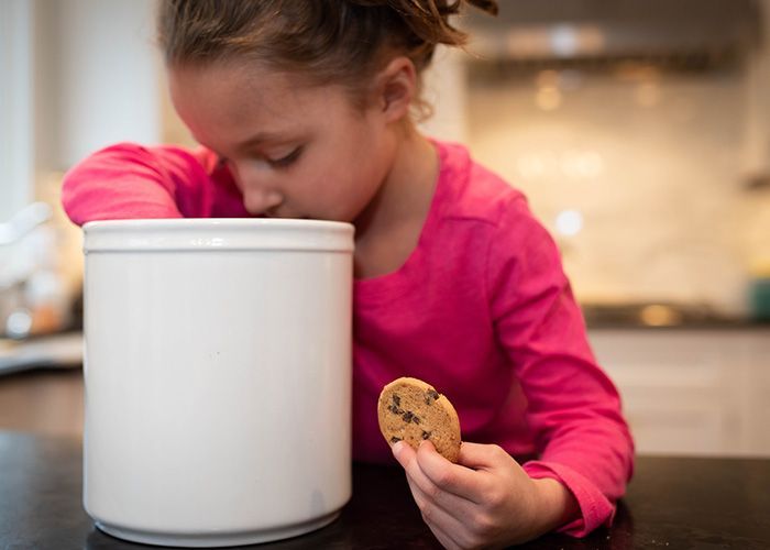 A little girl is eating a cookie from a cookie jar.