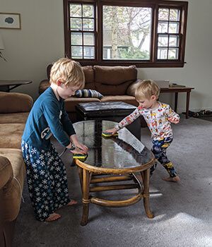 Two young boys are cleaning a coffee table in a living room.