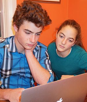 A boy and a girl are looking at a laptop computer.