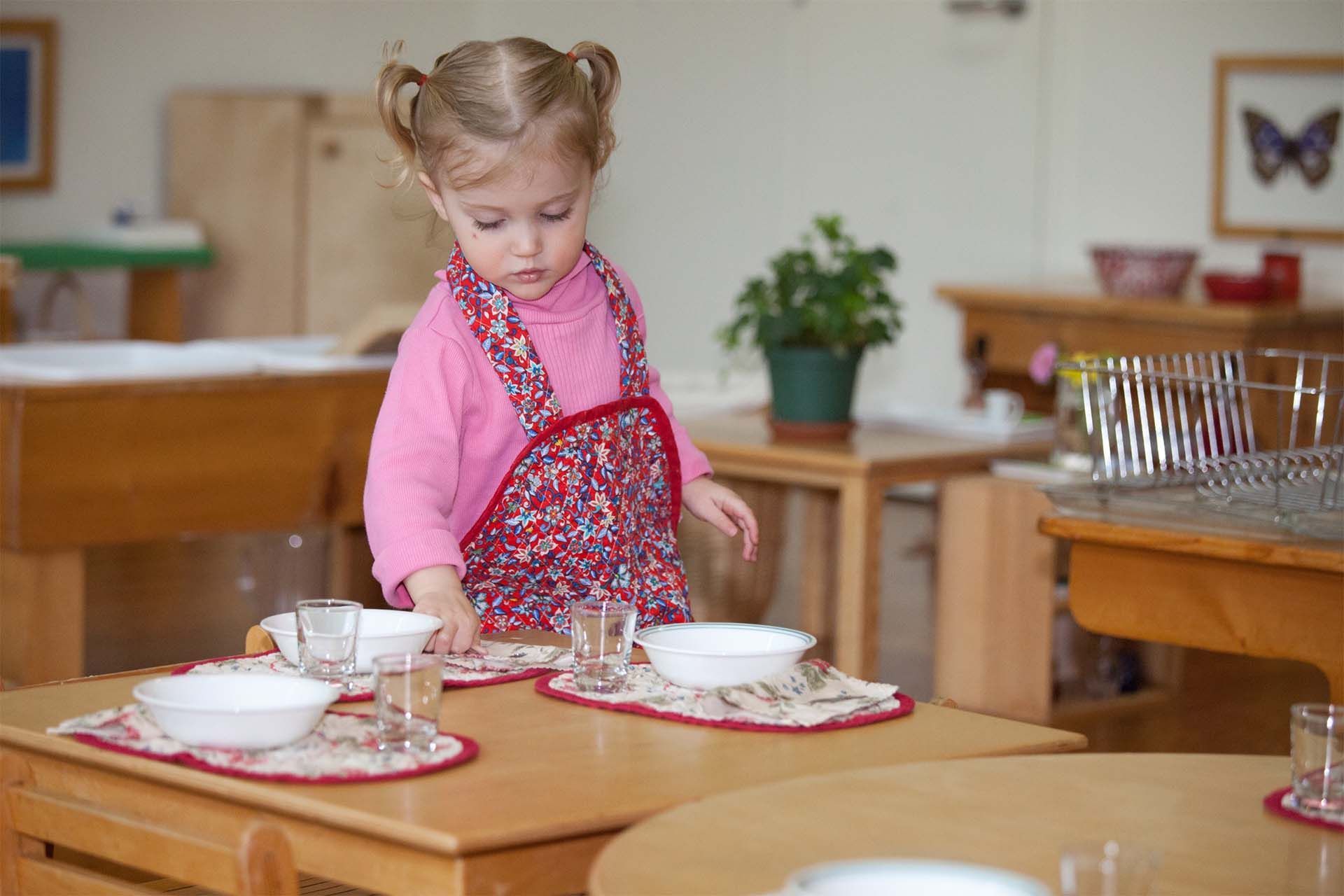 Montessori child is standing at a table with bowls and glasses.