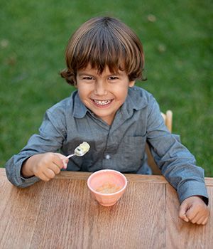 A young boy is sitting at a table eating food from a bowl with a spoon.