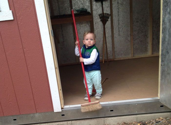 A little boy is standing in a doorway holding a broom.