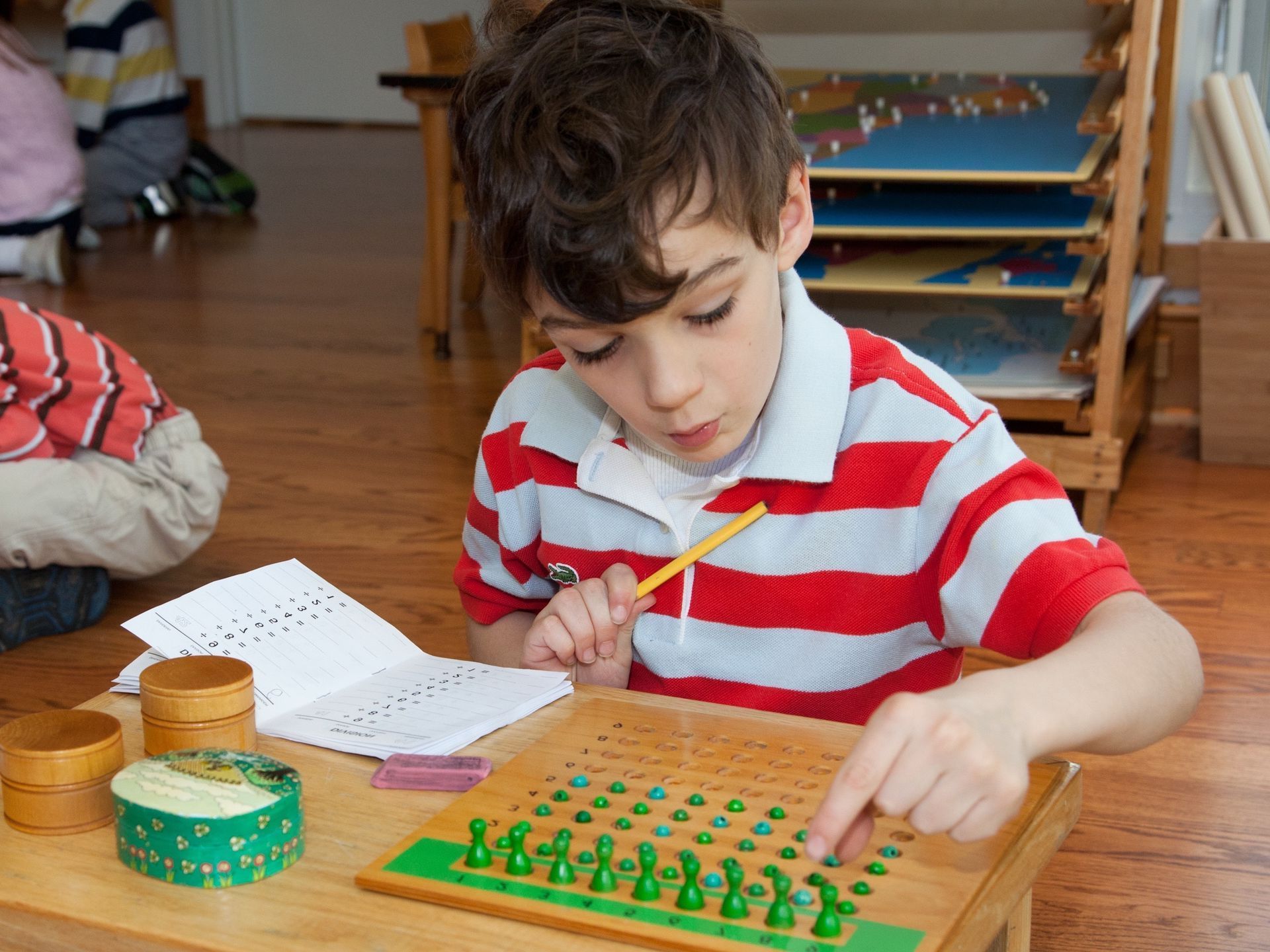 A Montessori child is sitting at a table working on a peg board