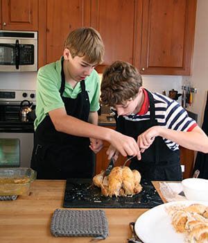 Two young boys are carving a turkey in a kitchen