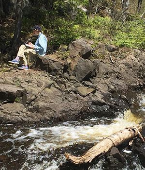 A man is sitting on a rock next to a river.