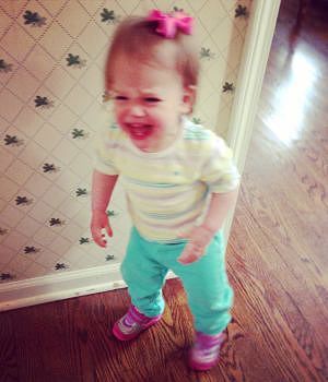 A little girl with a pink bow in her hair is standing on a wooden floor crying