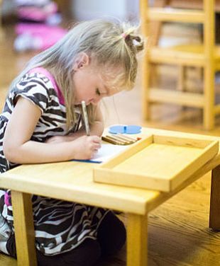 A little girl is sitting on the floor writing on a piece of paper.