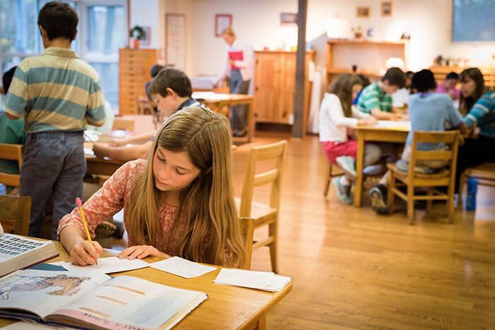 A girl is sitting at a table in a classroom with other children.