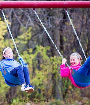 Two young girls are sitting on swings in a park.