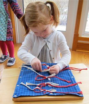 A little girl is sitting at a table playing with ribbons