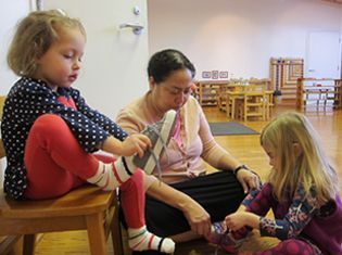 A woman is helping two little girls put on their shoes.