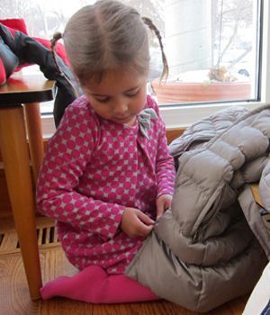 A little girl in a pink dress is sitting on the floor playing with a blanket