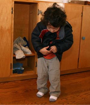 A young boy is putting on a jacket in front of a closet