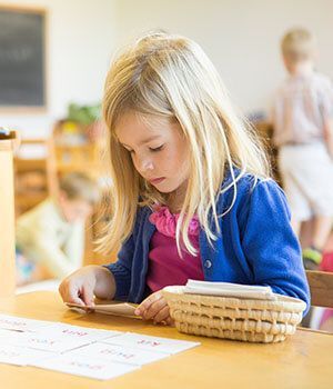 A little girl is sitting at a table looking at a piece paper cards.