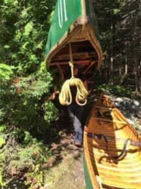 A person is carrying a canoe on a rope in the woods.