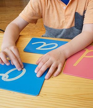 The hands of a boy running the finger over a letter on a paper card Montessori style.