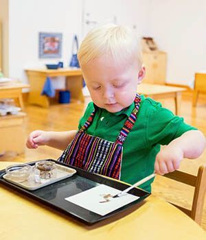 A young boy in an apron is sitting at a table playing painting on a paper