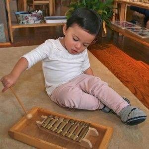 A little girl is sitting on the floor playing a xylophone.