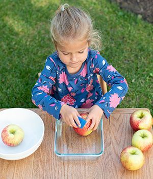 A little girl is cleaning an apple on a table.