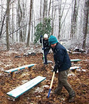 Two kids are shoveling dirt in the woods near benches.